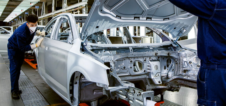 Two Asian workers are working on a car production line.