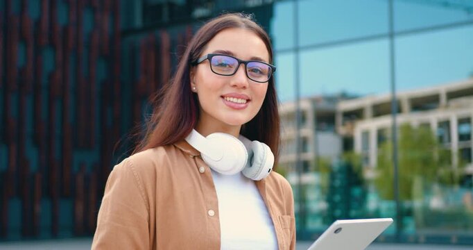 Close-up of Caucasian brunette woman in a blue shirt working on a wireless laptop outdoors in a city park, with a modern building in the background. Concept of remote work and people