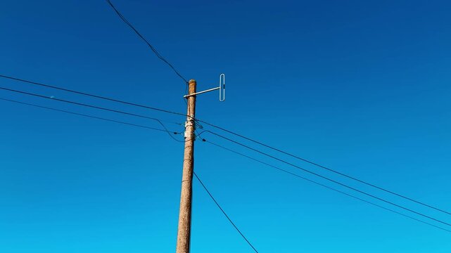 Old wooden antenna on pole against clear blue sky, weathered wood post with thin wires stretching across frame, rooftop edge