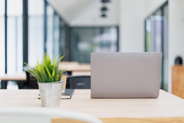 Fototapeta premium Employee working remotely at a modern office coworking space, desk with laptop, coffee, notebook, and a small plant, concept of freelance and business