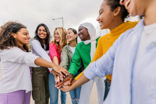 Diverse women standing together stacking hands outdoors. Confident young women showing mutual support and friendship. Empowerment and unity concept.