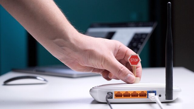 Person's hand placing a miniature stop sign on a white wifi router, symbolizing internet blocking, digital detox, parental controls, or limiting online access