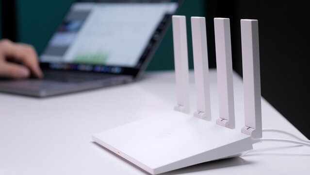 White wi fi router providing high speed internet access on a desk, with a person's hand typing on a laptop in the background, symbolizing remote work and digital connectivity