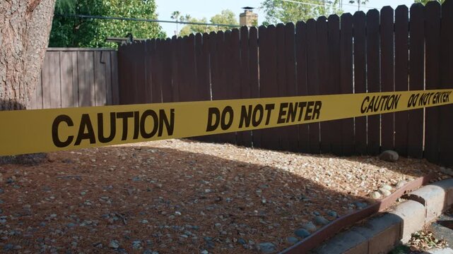Yellow caution tape do not enter across private backyard fence daytime shows restricted access area control and private property security in outdoor environment
