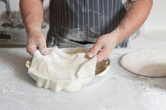 Hands stretching and placing phyllo dough into a baking tray. Traditional homemade pie preparation process in kitchen, rustic cooking scene.