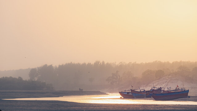 Traditional fishing boats anchored in a sunlit estuary river bank during golden hour with serene coastal landscape