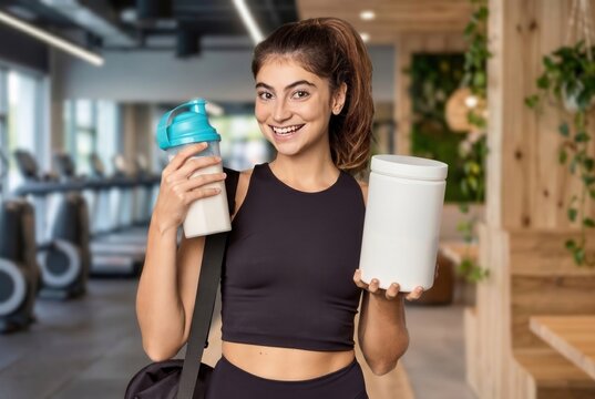 Woman standing in a gym, holding a shaker and a protein supplement container