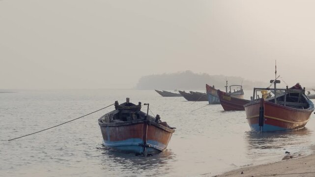 Wooden fishing boats anchored along a tranquil shoreline of talsari odisha at sunrise