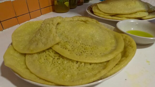 Moroccan baghrir pancakes served with olive oil, showing soft porous texture and golden surface. Traditional semolina crepes absorbing oil, offering a rich and savory twist on a classic dish.