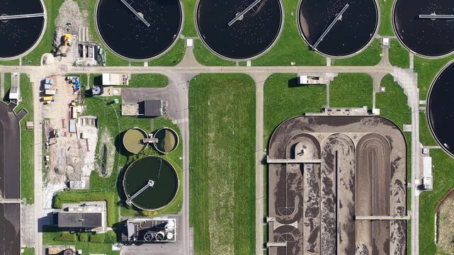High angle aerial perspective showing the modern infrastructure of a sewage and wastewater treatment plant, with circular clarifiers and aeration tanks processing and purifying water for recycling
