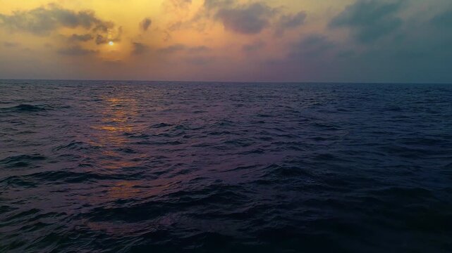 Golden sunset over the open ocean with dramatic clouds and gentle waves