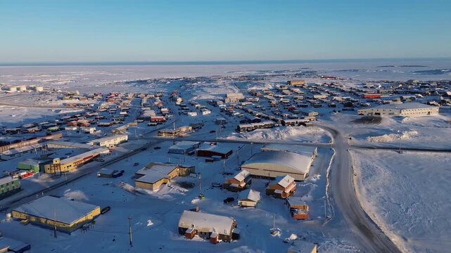 Drone pull-away shot above the massive stone Inuksuk at sunset, revealing the town of Rankin Inlet (Kangiqliniq) and the Arctic landscape.