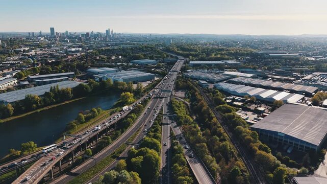 Side aerial drone footage flying along a motorway with an exit ramp in Birmingham, United Kingdom. Traffic moving past a lake with city skyline in the background.