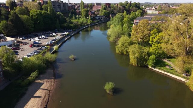Drone flying directly over Welsh Bridge and River Severn in Shrewsbury, UK. Cars crossing stone arch bridge, lush green riverside park and Georgian town visible.