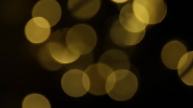 Abstract golden bokeh lights float and shift slowly across dark background as circles expand and drift creating smooth motion and warm festive atmosphere suitable for holiday or ambient visuals