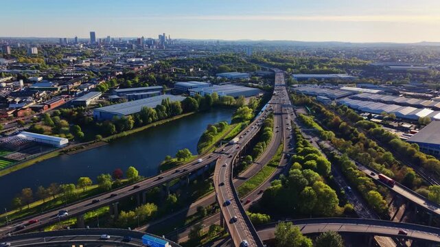Drone pulling back to reveal Spaghetti Junction M6 interchange, Birmingham city skyline, river and green suburbs. Golden sunset light. Stunning wide establishing shot.
