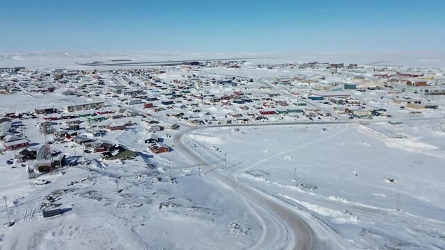 A wide drone shot with a slight rightward movement showing the town of Rankin Inlet (Kangiqliniq) with the Rankin Inlet Airport (YRT) runway and infrastructure visible in the background.