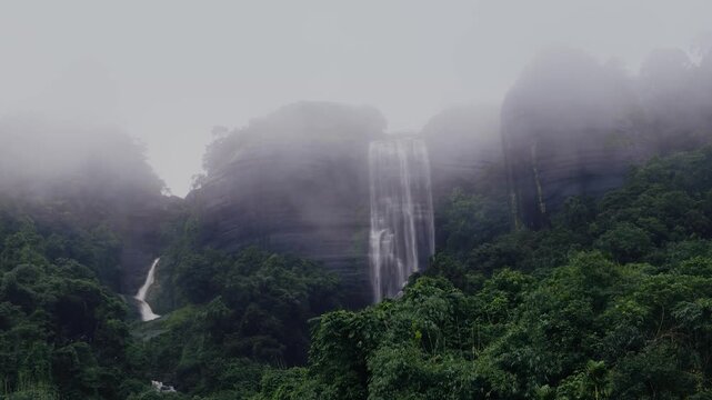 Misty waterfall cascading through lush rainforest cliffs in Meghalaya during monsoon season