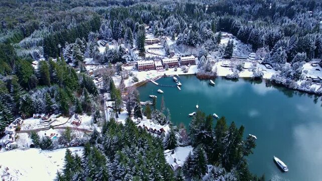 Drone moving forward while tilting camera up to reveal a luxury lakeside resort, moored boats, and the snow-capped Andes mountains on Nahuel Huapi Lake, Patagonia National Park.