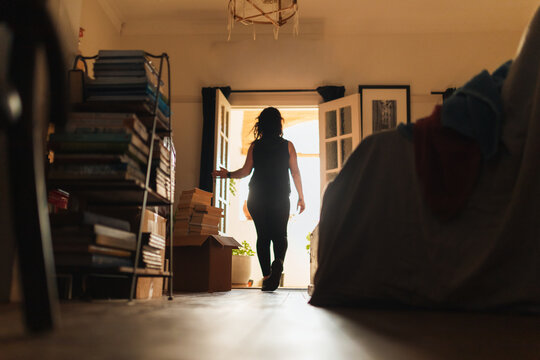 Woman walking through bright open doorway with books and boxes, preparing for a move