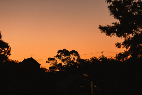 A hillside church with a cross silhouetted against a vibrant orange sunset sky