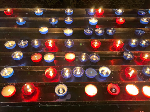 Rows of lit red and blue votive candles in a church interior create a devotional atmosphere, symbolizing prayer, remembrance, and quiet reflection.
