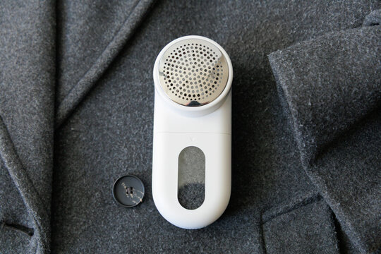 Lint remover on gray coat with fabric pills, clothes care tool removing fuzz from wool surface