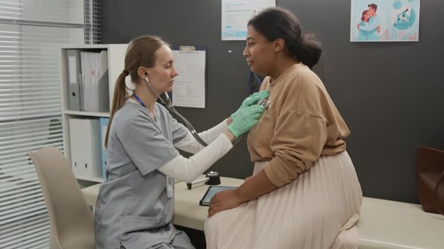 Female doctor checking lungs of patient using stethoscope and speaking to her after finishing health checkup in clinic