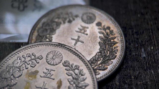 Close up video of the reverse side of a Japanese Meiji 50 sen coin, featuring the central denomination, imperial chrysanthemum crest, and ornamental wreath design.