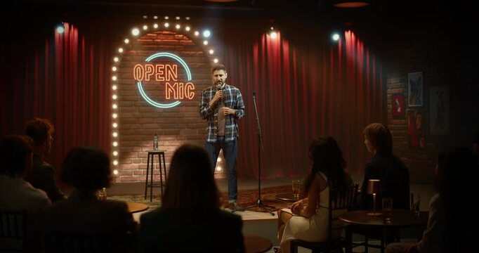 Male Comedian Performs a Witty Stand-up Routine at an Open Mic Night, Delivering Punchlines on Stage as the Crowd Listens, Laughs, and Enjoys a Lively Live Comedy Show in a Bar Club.