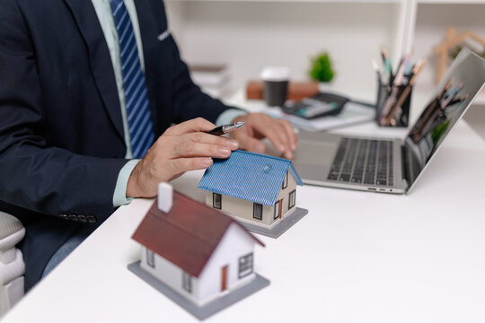 Real estate agent presenting house model during online meeting on laptop, explaining property investment and home buying options, representing sales communication and professional service.