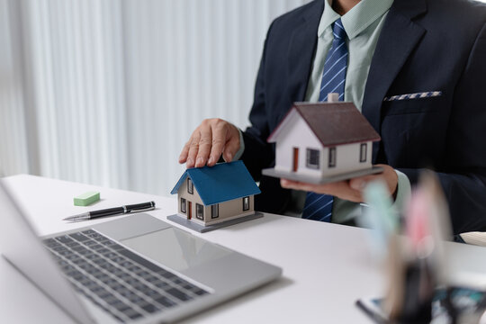 Real estate agent presenting house model during online meeting on laptop, explaining property investment and home buying options, representing sales communication and professional service.