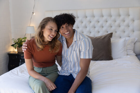 Couple sitting on bed leaning toward each other, smiling near tufted headboard and string lights