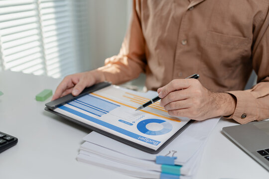 Person reviewing budget report and financial data on documents, analyzing charts and numbers, representing accounting work, financial planning, and business decision making.
