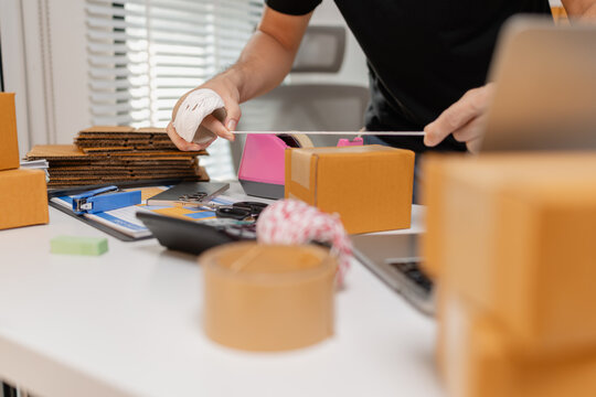 Small business owner tying parcel with string while preparing package for delivery, organizing shipping process and handling ecommerce orders, representing logistics and packaging workflow.