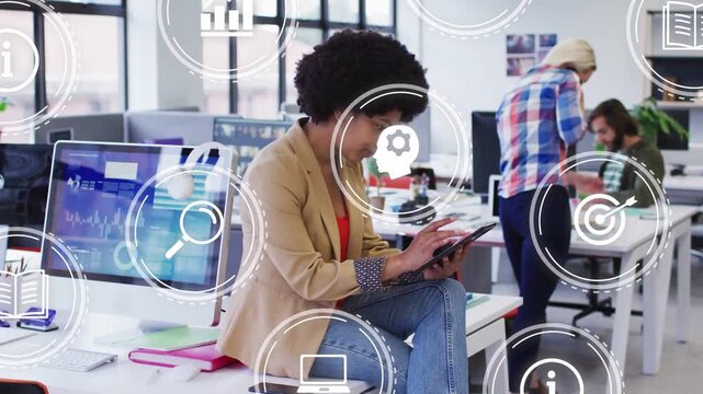 Sitting woman tapping tablet in office causing UI icons over charts while team discussing data