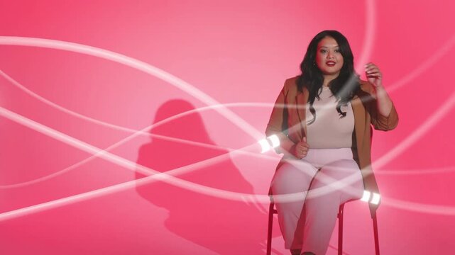 Model sitting on stool in pink set, light trails sweeping over her, initiating gestures for ads