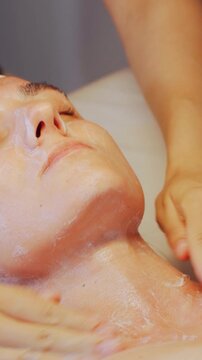 Beauty care routine, vertical video. Skincare professional thoroughly performs facial cleansing and relaxing massage. Skincare expert carries out facial cleaning followed by soothing massage session