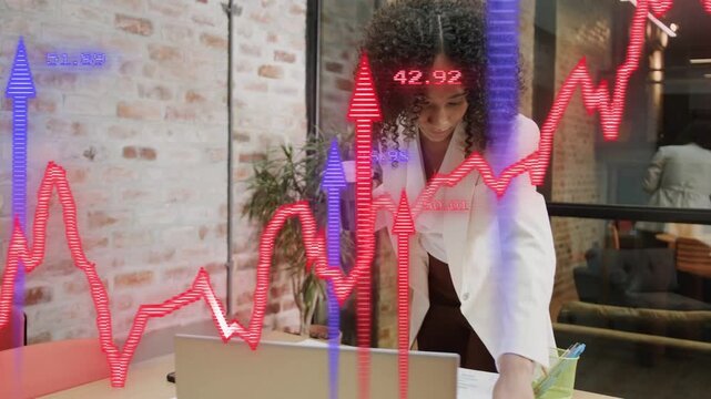 Woman placing paper by laptop, causing finance charts overlay, checking totals and switching focus