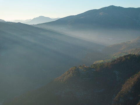 Mountain landscape with sun rays shining through fog, creating a tourism destination concept in Luserna, Alpe Cimbra, Trentino, Italy.