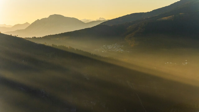 Mountain landscape at sunrise with fog and sun rays over a village, tourism concept, Luserna, Alpe Cimbra, Trentino, Italy.