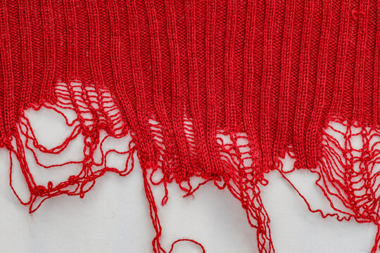 Knitting project with red yarn showing uneven edges and loose threads requiring repair in workshop setting