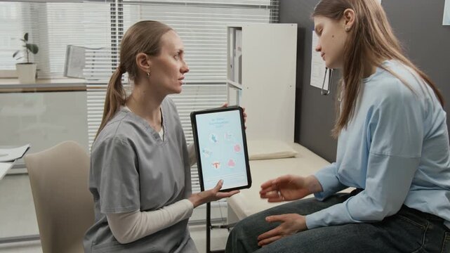 Gen Z girl sitting on medical couch listening to female doctor telling her about IVF treatment during preconception consultation in fertility clinic