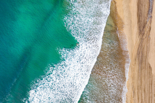 Drone aerial view of a sandy beach and blue sea captured from above on a hot summer day. The composition shows the meeting of shoreline and water with vibrant colors and natural patterns. Perfect conc