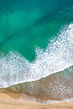 Drone aerial view of a sandy beach and blue sea captured from above on a hot summer day. The composition shows the meeting of shoreline and water with vibrant colors and natural patterns. Perfect conc