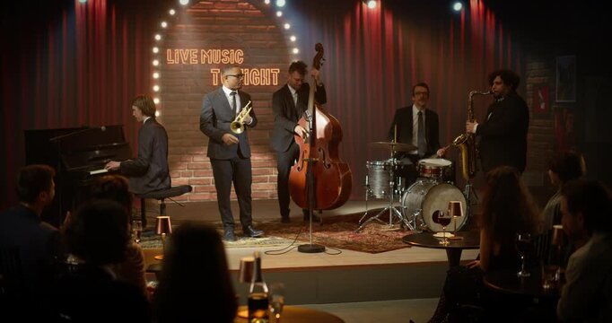 A Black Male Trumpeter Fronts a Live Jazz Band Playing an Energetic Song on a Bar Stage During a Concert Event, Joined by Piano, Upright Bass, Drums and Saxophone as the Audience Watches Closely.