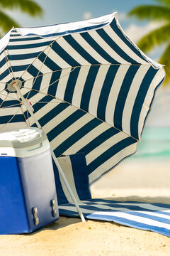 Beach umbrella and portable cooler placed on hot sandy beach under bright sunlight. The scene captures relaxed summer atmosphere with clear blue sky and seaside vibes. Summer and vacation concept.