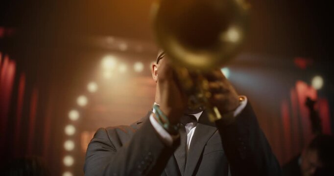 Portrait Black Male Trumpeter in Glasses Leads Live Jazz Band Concert at a Bar, Playing a Powerful Song on Stage as the Audience Enjoys the Music Event and Follows His Dynamic Solo Performance.