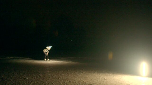 Night performer with glowing staff near lamp. Solitary urban artist spins staff in low light, steps back into shadow, sweeps arcs of firelike glow, crouches to adjust prop