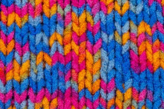 Colorful knitting pattern shows interwoven threads in bright shades such as pink, blue, orange, and yellow in a close view